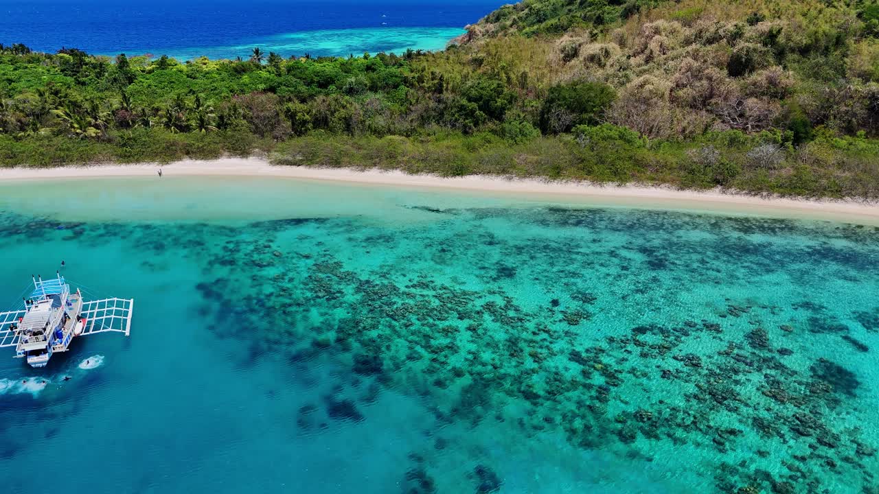 Drone footage of a beach and turquoise lagoon near Palawan in the Philippines with boats and swimmers