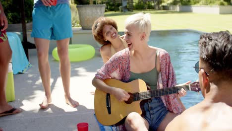 happy diverse group of friends playing guitar at pool party in summer