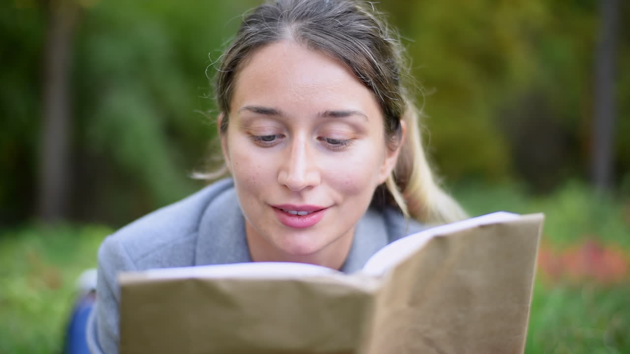 Blonde woman reading a book, lying on the grass in a park