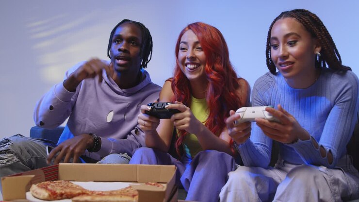Gruppo di amici della Gen Z seduti sul divano a casa che giocano e mangiano pizza d'asporto