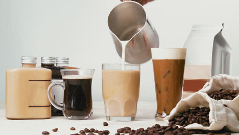 pouring fresh steamed milk into a glass half-filled with brewed coffee