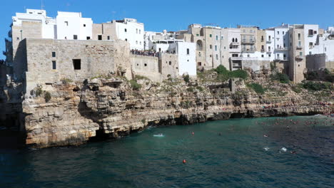 Drone-shot-of-a-young-man-diving-off-the-cliffs-of-Lama-Monachile-in-Puglia,-Italy