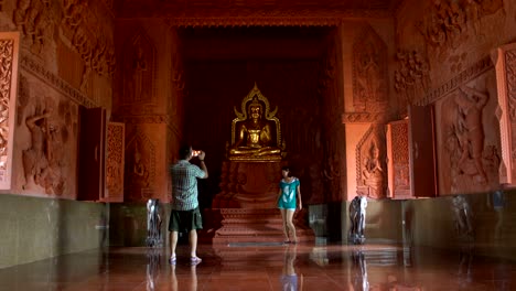 a man is photographing a woman at a smartphone by a buddha statue in a buddhist temple