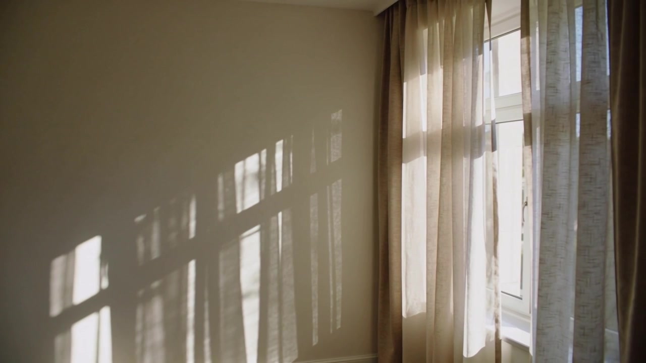 Shifting sun casting window shadows across pale wall in bedroom corner and sheer drapes drifting