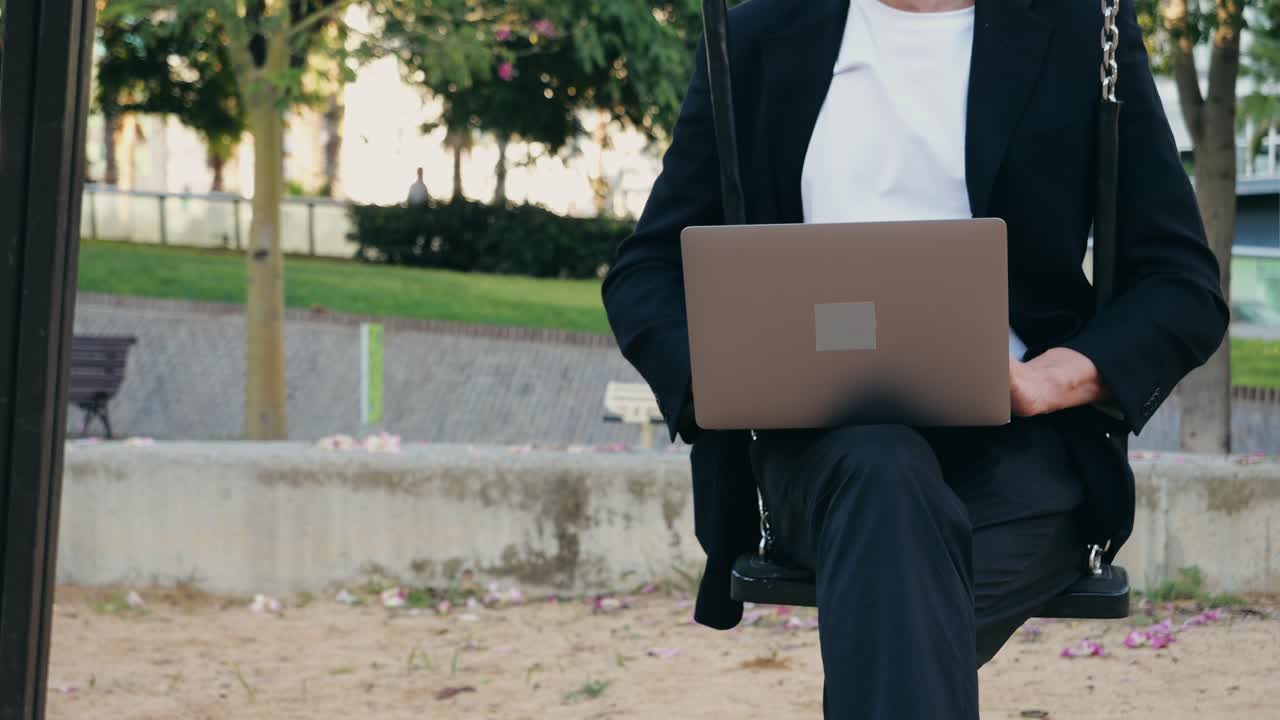 Man working on laptop while sitting on a swing in a park