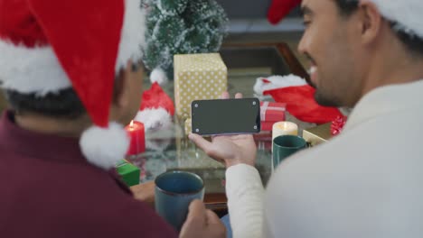 biracial adult son and senior father in santa hats making smartphone christmas video call