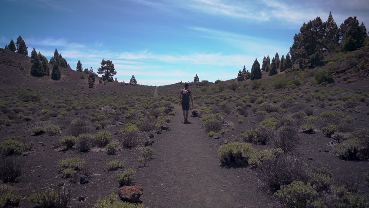 vista trasera de un joven europeo con camisa roja y mochila gris en un paisaje volcánico sigue el camino en la palma, ruta de los volcanes en las islas canarias