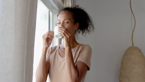 woman enjoying coffee by window, smiling and looking outside, at home