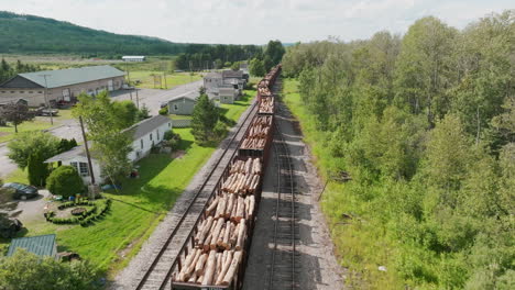 high aerial view of stationary freight train loaded with lumber, adjacent to residential homes in rural maine