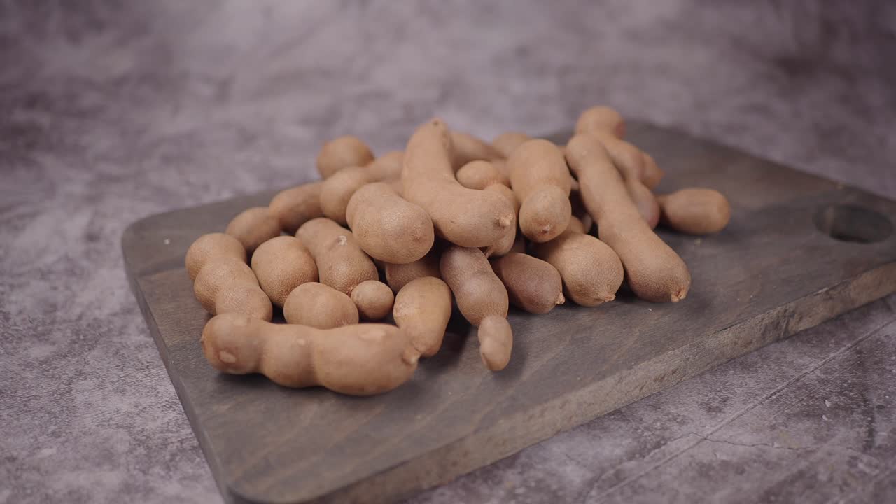 Mano che raccoglie baccelli di tamarindo freschi da una tavola di legno