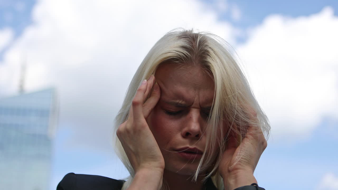 Young overworked businesswoman is having headache. She is suffering and pressing her head, while she is standing on street in city. Exhausted woman is having problem with concentration