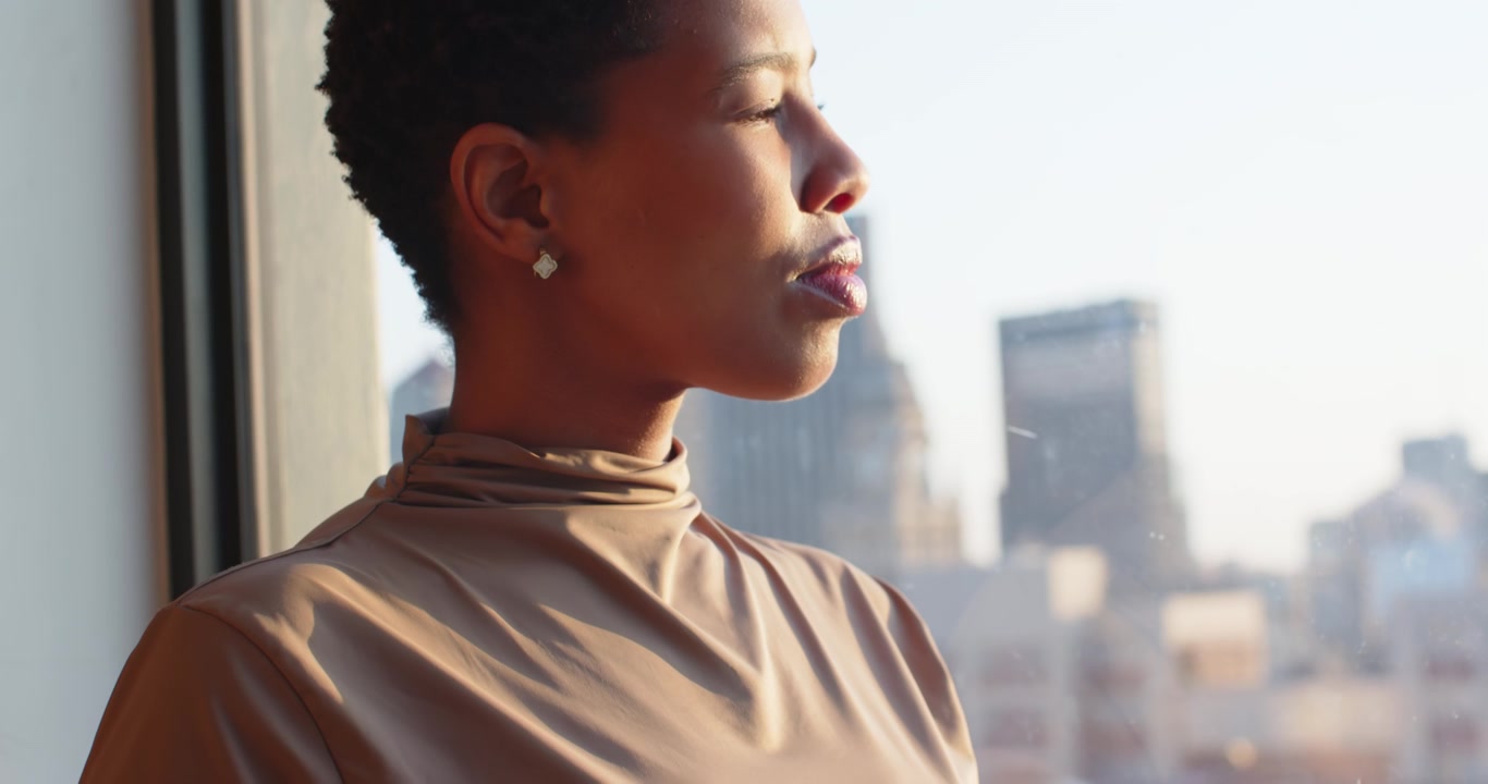 Warm sun drawing African American woman at window, closing eyes briefly, holding white mug for calm