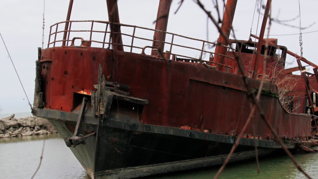 Rusty red shipwreck stuck in shallow green water