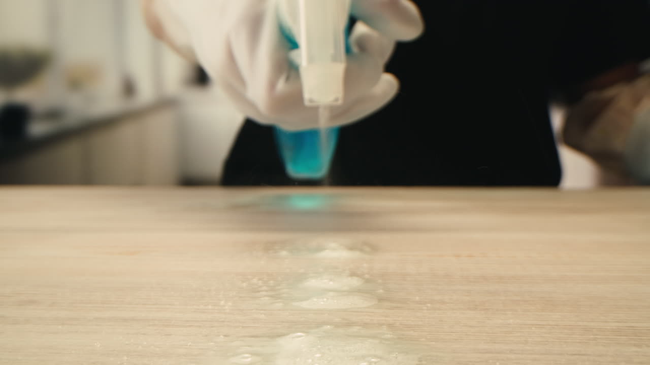 Gloved Hand Spraying and Wiping a Wooden Surface Clean