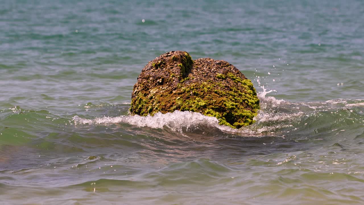 바다의 파도가 해변 한가운데의 바위에 부 ⁇ 히고