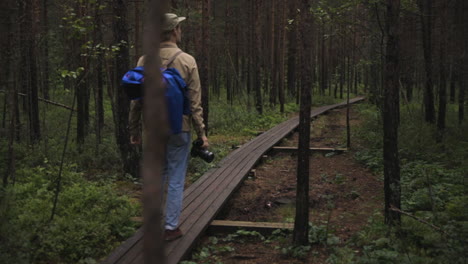 fotógrafo masculino camina por un camino de madera a través del bosque, cacerola lenta