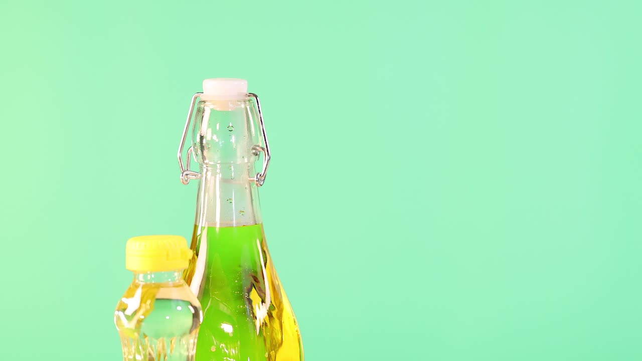 Bottles of various oils with coconuts and avocados against a bright green backdrop. Static composition with vivid lighting