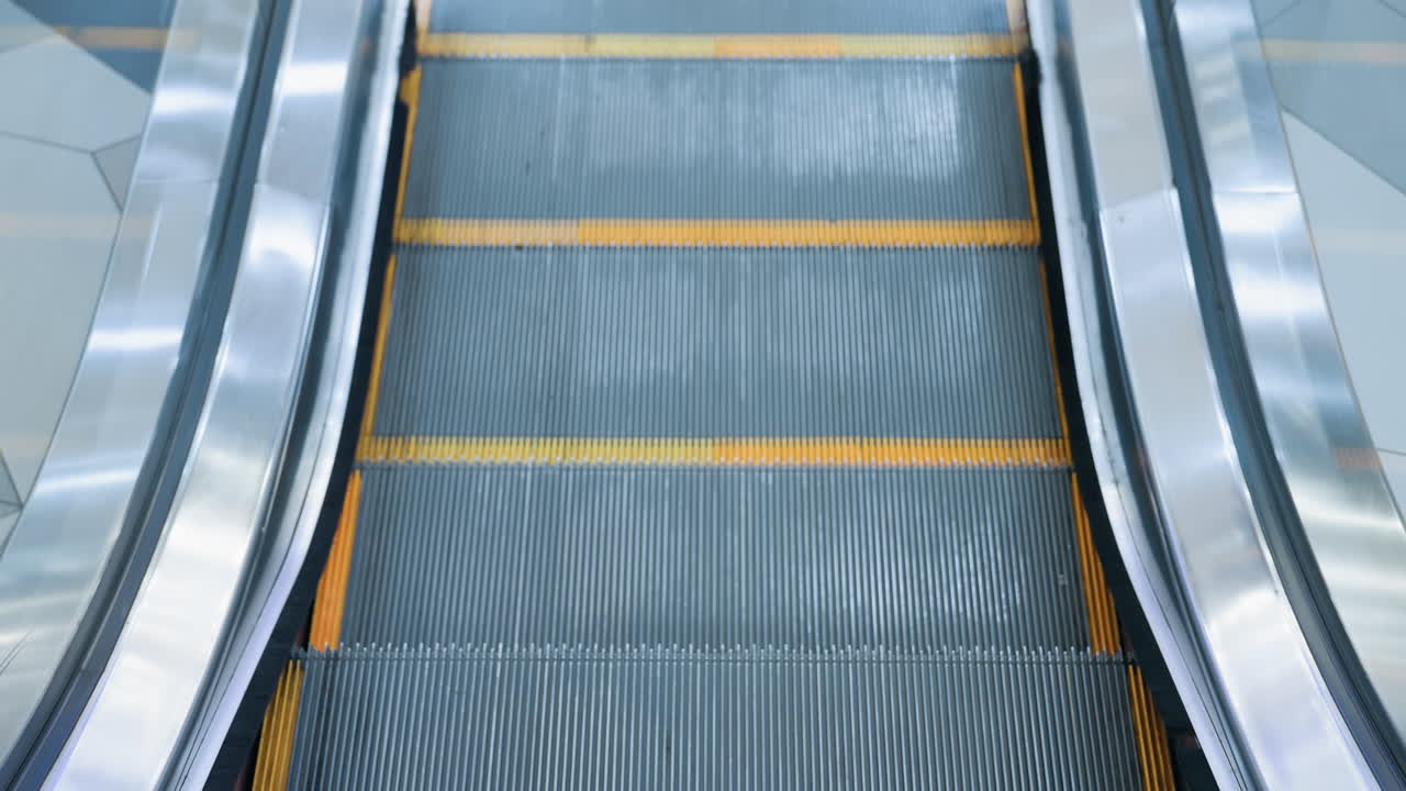 Upward-moving escalator with sleek glass frame, yellow markings, and reflective metal borders in a modern shopping mall, clean, polished design enhances the dynamic urban transport scene