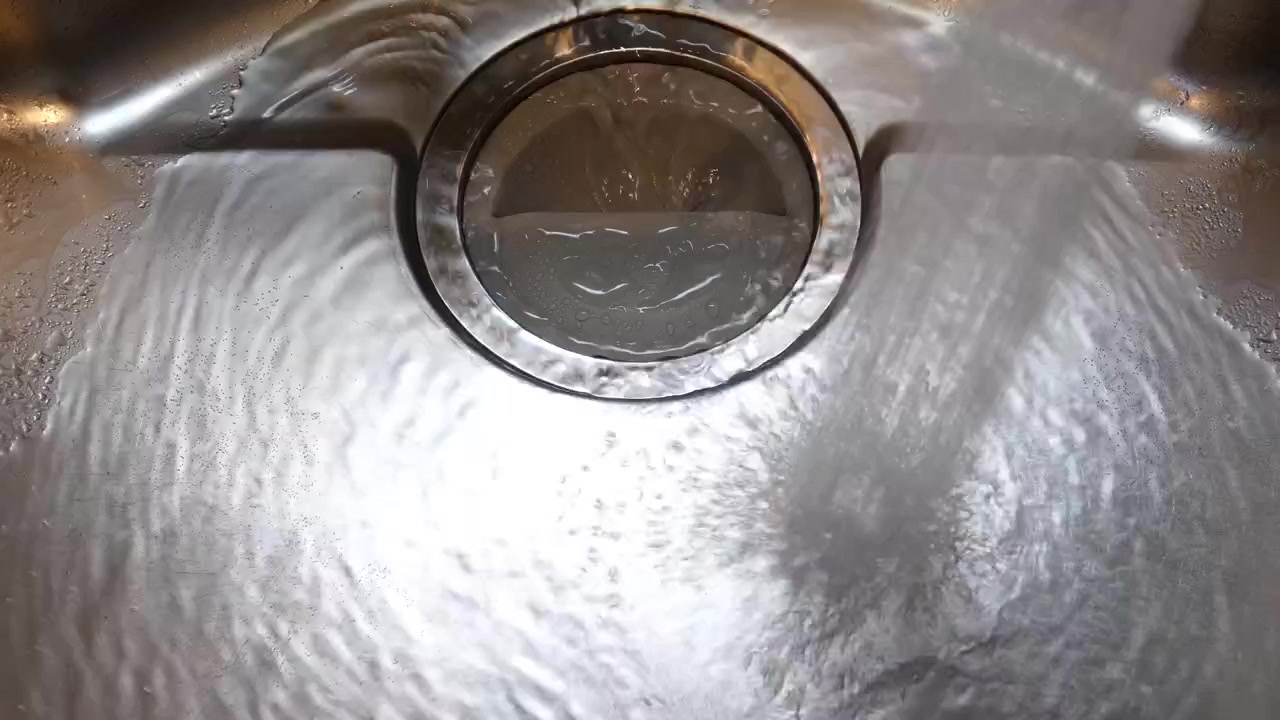 Close up of a kitchen sink with water going down the drain and then the tap-faucet turned off.