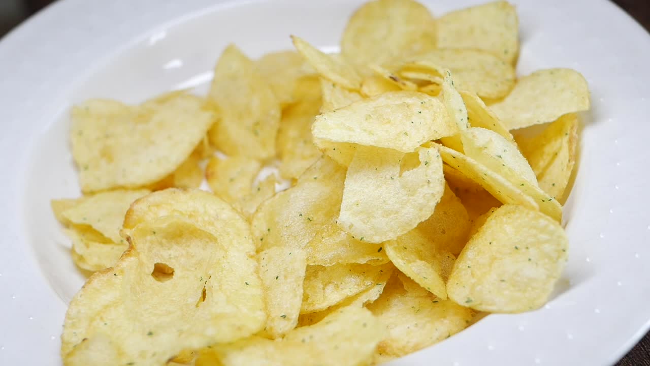 Hand Reaching for Crispy Potato Chips on a Plate