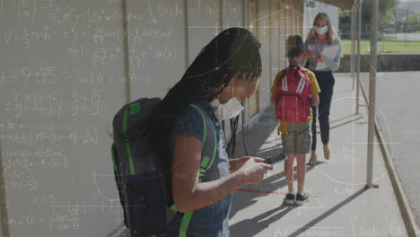 animation of mathematical equations over diverse schoolchildren and teacher wearing face masks