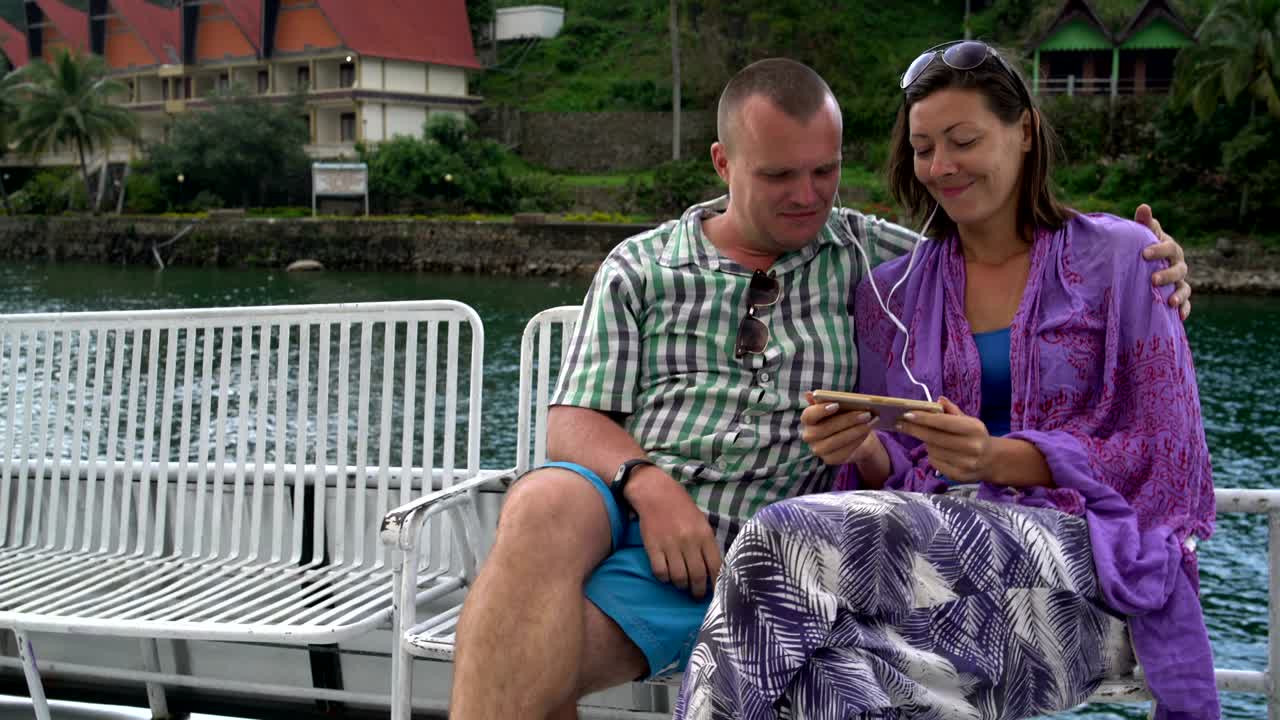 남자 와 여자 는 즐거움 의 배 에 있는 벤치 에 앉아 음악 을 듣고 있다