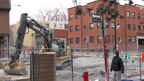 an excavator is working to repair a street in montreal. around you can see buildings and people passing by.