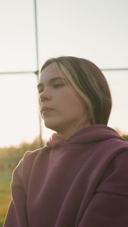 joven con capucha inclinándose ligeramente hacia adelante, aparentemente jugando un juego con la luz del sol que irradia desde la distancia, campo abierto en el fondo creando un entorno al aire libre pacífico y vibrante