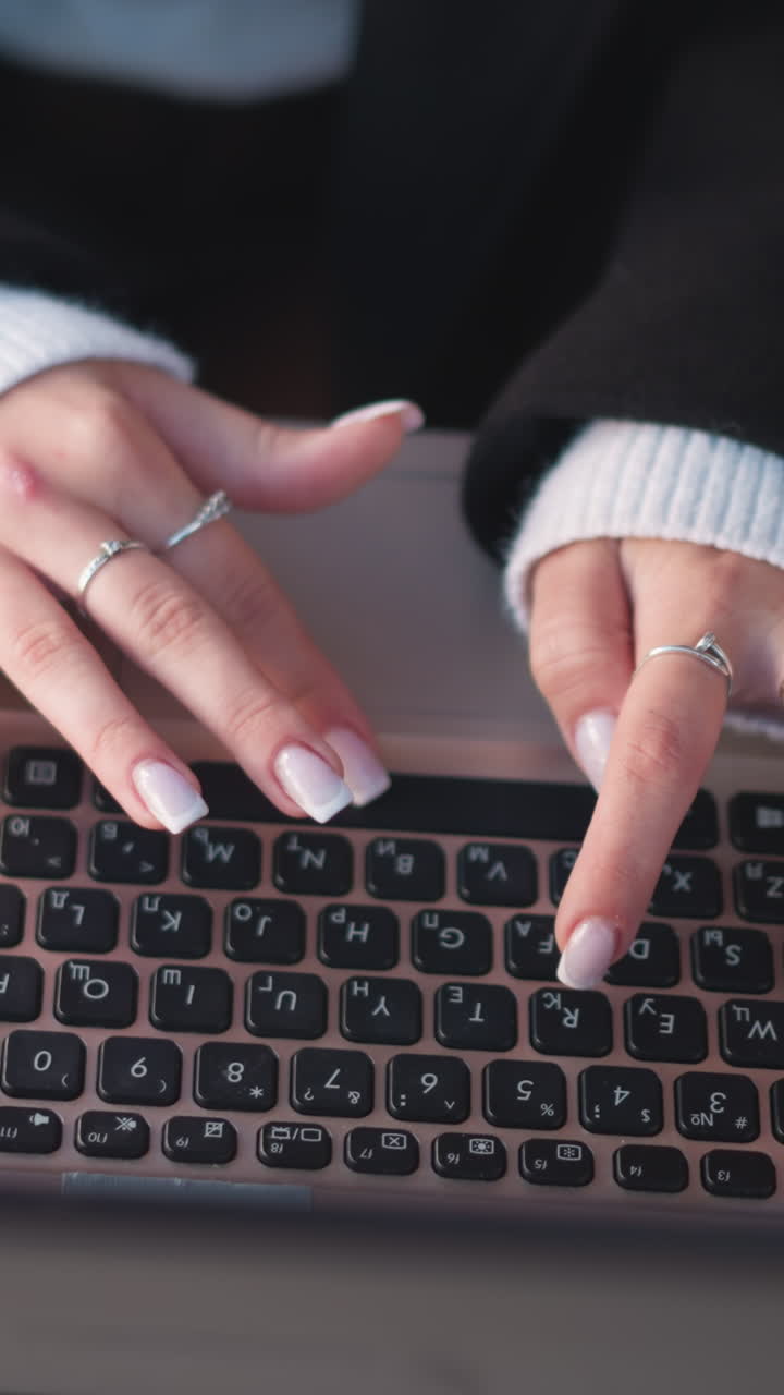 섬세한 반지와 은 손으로 장식된 손의 클로즈업, 노트북 키보드에서 야외에서 타이핑하고, 근처에 스마트폰이 있는 나무 테이블에 놓여 있습니다.
