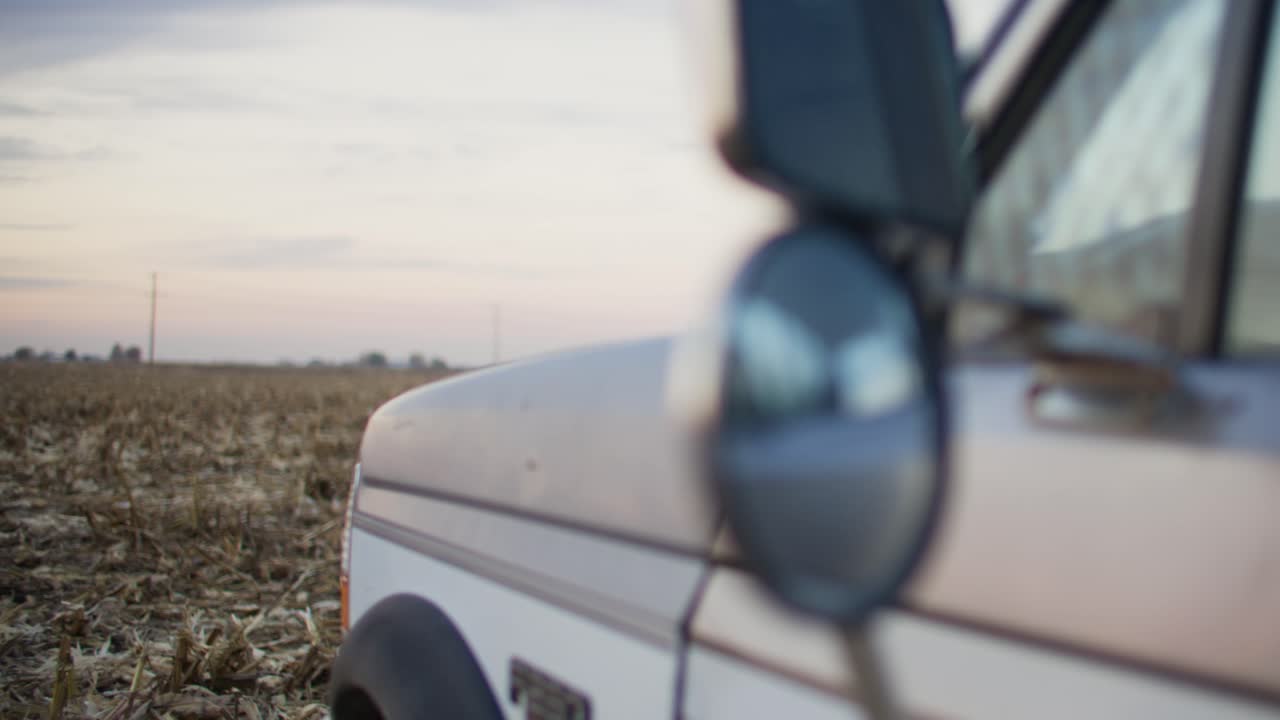 Mirror on an old blue truck sitting in a corn field during harvest season.