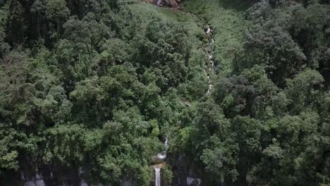 Vista-Aérea-De-Una-Alta-Cascada-Que-Cae-Por-Un-Acantilado-Rodeada-De-Exuberante-Vegetación-Verde.