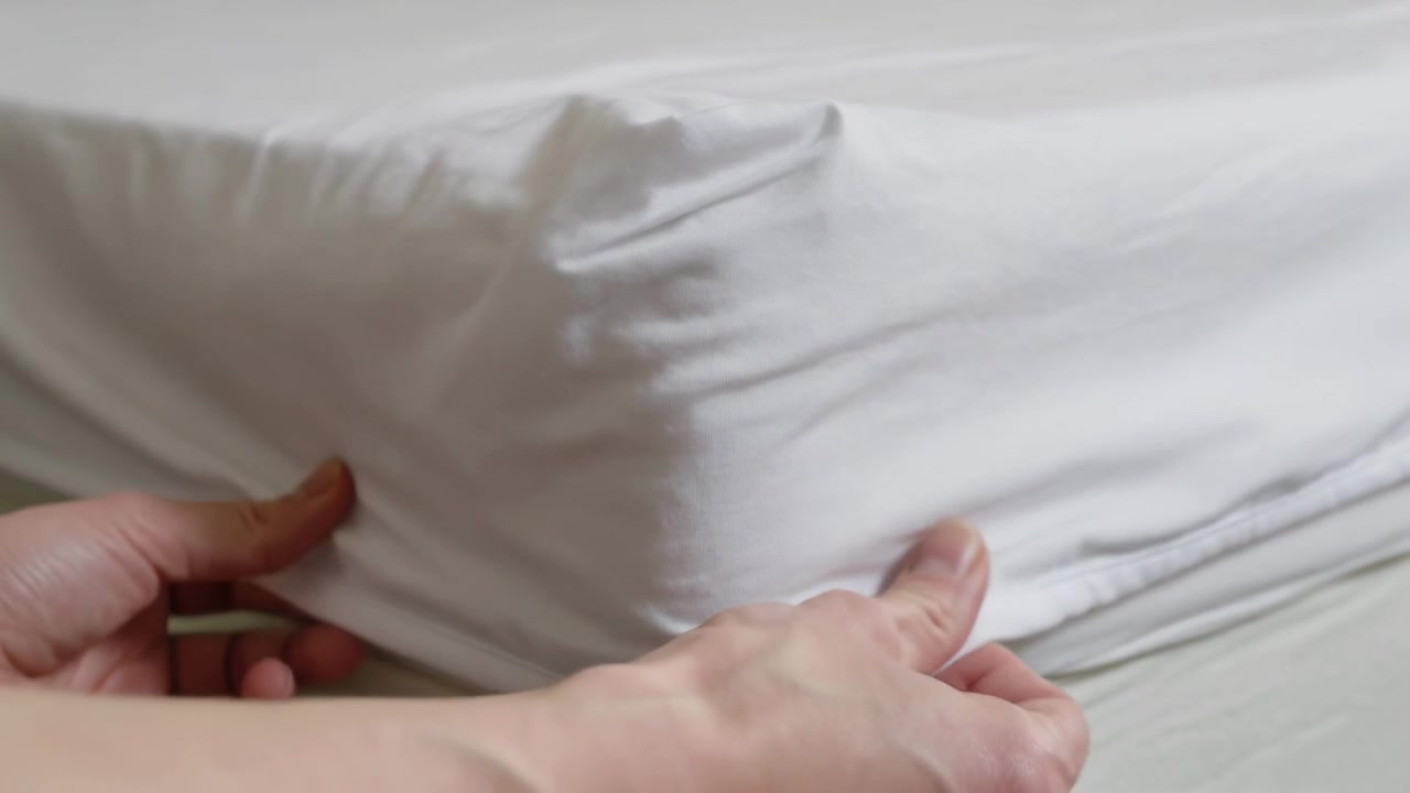 Sollevando il bordo, le mani tirano un lenzuolo elastico sull'angolo del materasso sul letto, lisciandolo per farlo aderire all'angolo.