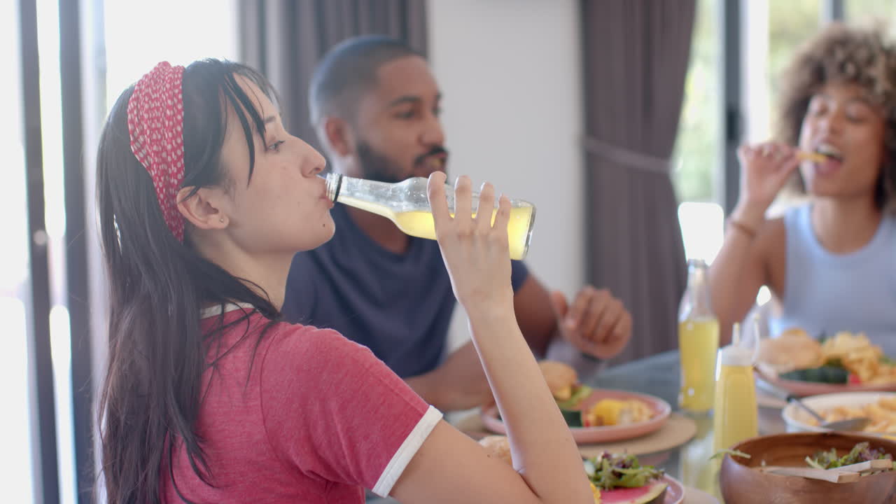 Diverse friends enjoying meal, woman drinking soda, others eating and chatting together