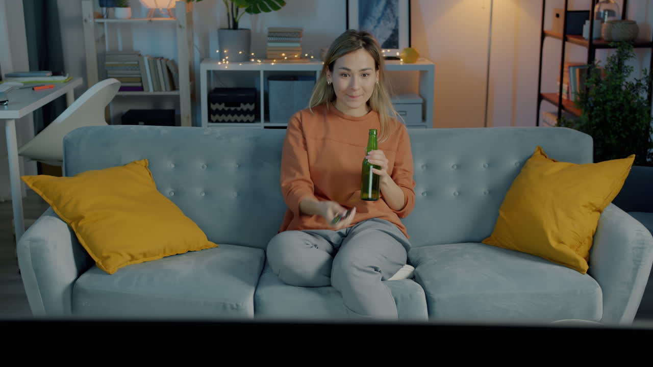 Kvinde ser tv og drikker øl på sofaen