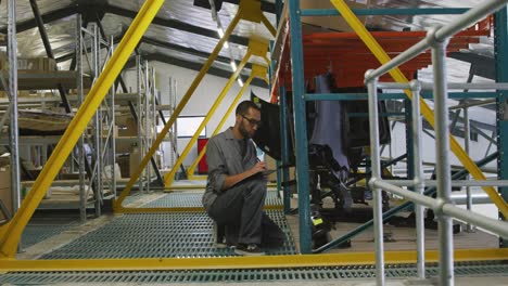 african american male car mechanic kneeling in a warehouse and using a tablet