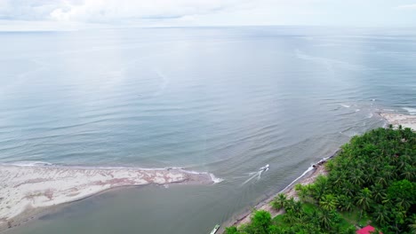 Boat-leaving-the-river-and-going-into-the-Ocean-next-to-small-coastal-village