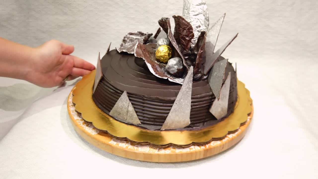 Primo piano di una torta al cioccolato con decorazioni geometriche mentre una mano di donna la ruota su un piatto.