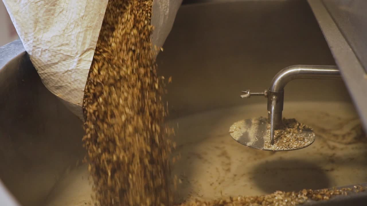 Pouring A Bag Of Malt Grains Into The Crushing Machine In A Brewery For Milling - close up slowmo