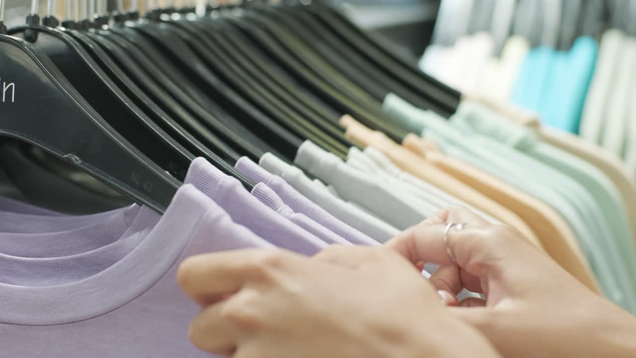 Close-up of female hands plucked a hanger with clothes. Woman's hands run across a rack of clothes. Dolly shot from the side. Woman's hand smoothing a colorful clothes. Close-up: a hanger for clothing