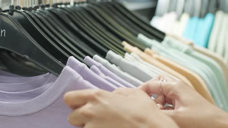 close-up of female hands plucked a hanger with clothes. woman's hands run across a rack of clothes. dolly shot from the side. woman's hand smoothing a colorful clothes. close-up: a hanger for clothing