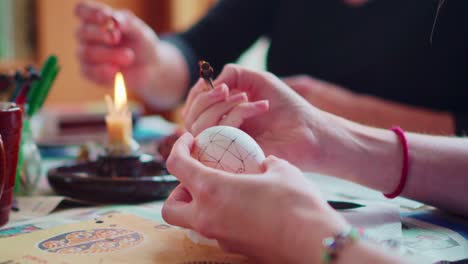 primer plano de las manos de los artistas dibujando diseños ornamentados tradicionales en huevos de pascua con lápiz