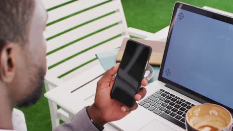 Midsection-of-african-american-businessman-using-smartphone-and-laptop-in-cafe