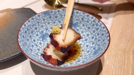 chopsticks lifting octopus with wasabi from bowl