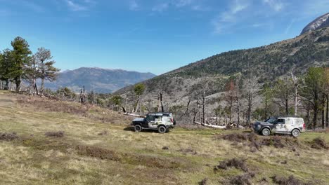 aerial shot of two cars driving along mountain side with mountain peak on background