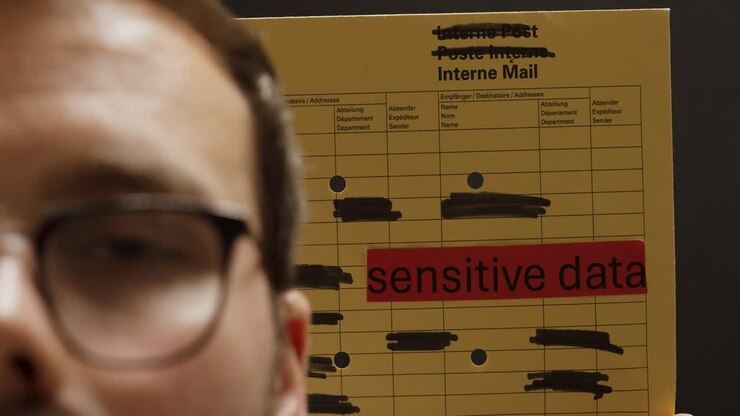 En mand holder en intern postkuvert mærket “sensitive data” og understreger vigtigheden af fortrolighed og korrekt datahåndtering på arbejdspladsen.