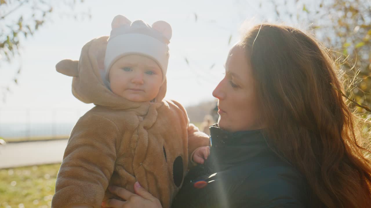 Ein herzerwärmender Moment eines fröhlichen Kindes in einem gemütlichen Outfit, das seine Mutter an einem sonnigen Tag im Freien anlächelt und dabei die Essenz von familiärer Liebe und Verbundenheit einfängt