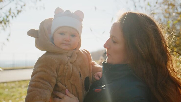 Ein herzerwärmender Moment eines fröhlichen Kindes in einem gemütlichen Outfit, das seine Mutter an einem sonnigen Tag im Freien anlächelt und dabei die Essenz von familiärer Liebe und Verbundenheit einfängt