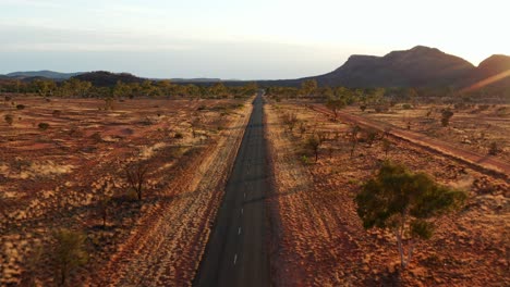 Vista-Aérea-De-La-Carretera-Interior-En-Medio-Del-Desierto-Al-Atardecer-Cerca-De-La-Ciudad-De-Alice-Springs-En-Australia