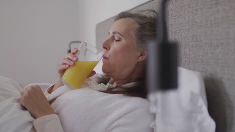 sick woman drinking juice while lying in bed at home