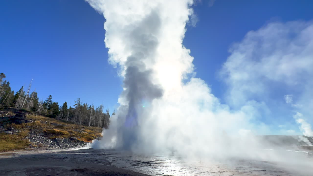 Cinematic Grand geyser Old Faithful sun glare sunrise sunset eruption explosion steam Yellowstone National Park observation deck Upper Geyser Basin fall autumn beautiful blue sky slow motion still